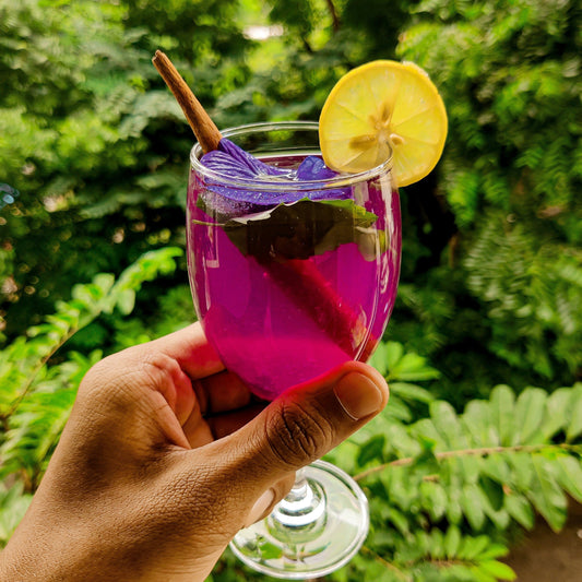 Butterfly pea flower tea in glass showing purple magenta color with lemon slice and cinnamon stick
