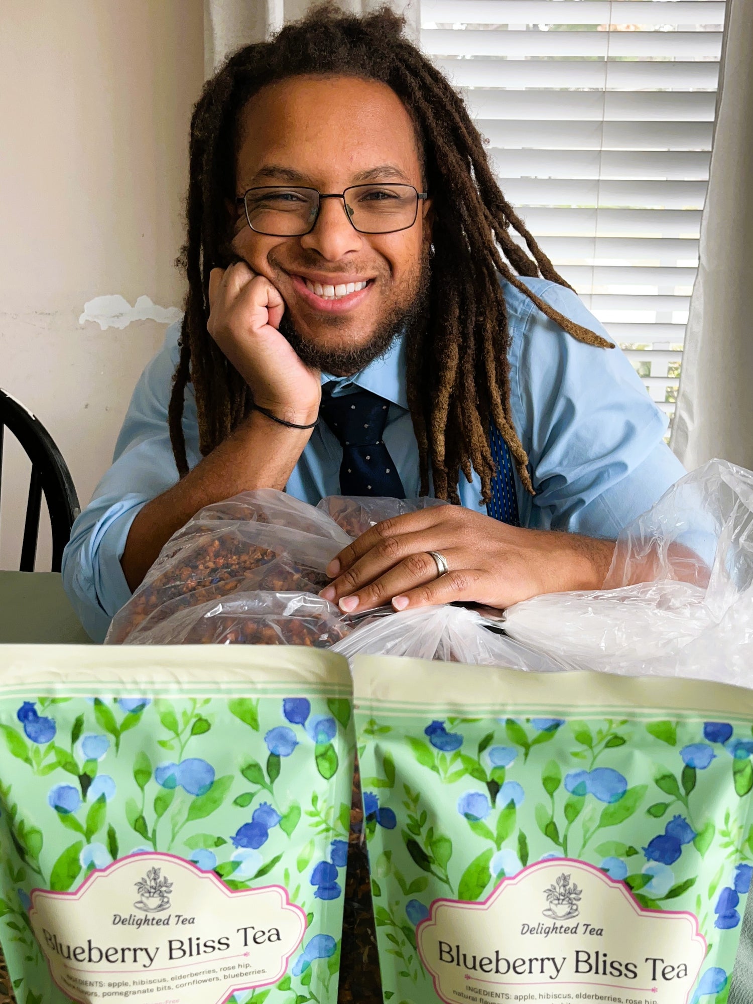 Jeremy with dreadlocks sitting behind two bags of Blueberry Bliss Tea