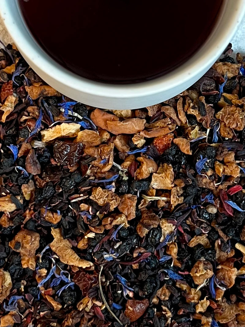 Tea leaves with a cup of black tea in the background