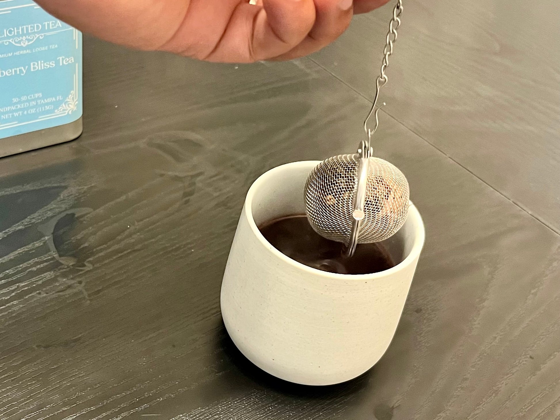 Tea ball being added to a cup of tea on a wooden surface
