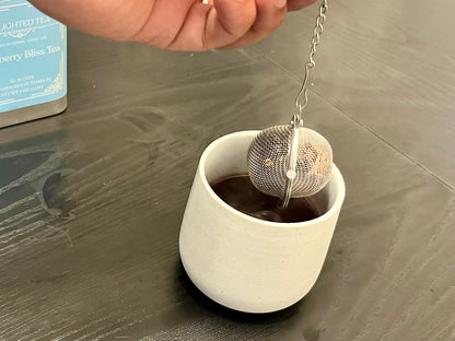 Tea ball being added to a cup of tea on a wooden surface