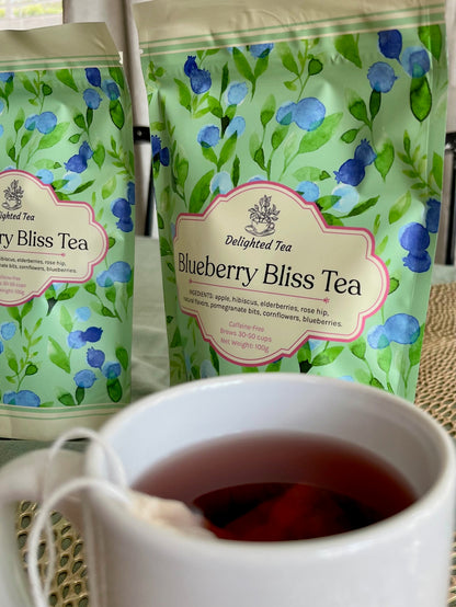 Two packages of Delighted Tea Blueberry Bliss Tea with a cup of tea in the foreground.