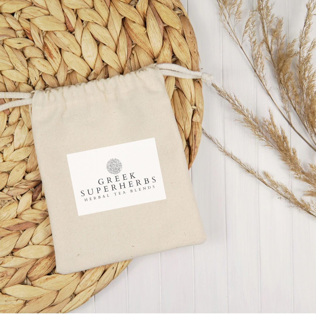 Cotton pouch with Greek Superherbs label on a woven mat with dried herbs.