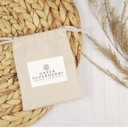 Cotton pouch with Greek Superherbs label on a woven mat with dried herbs.
